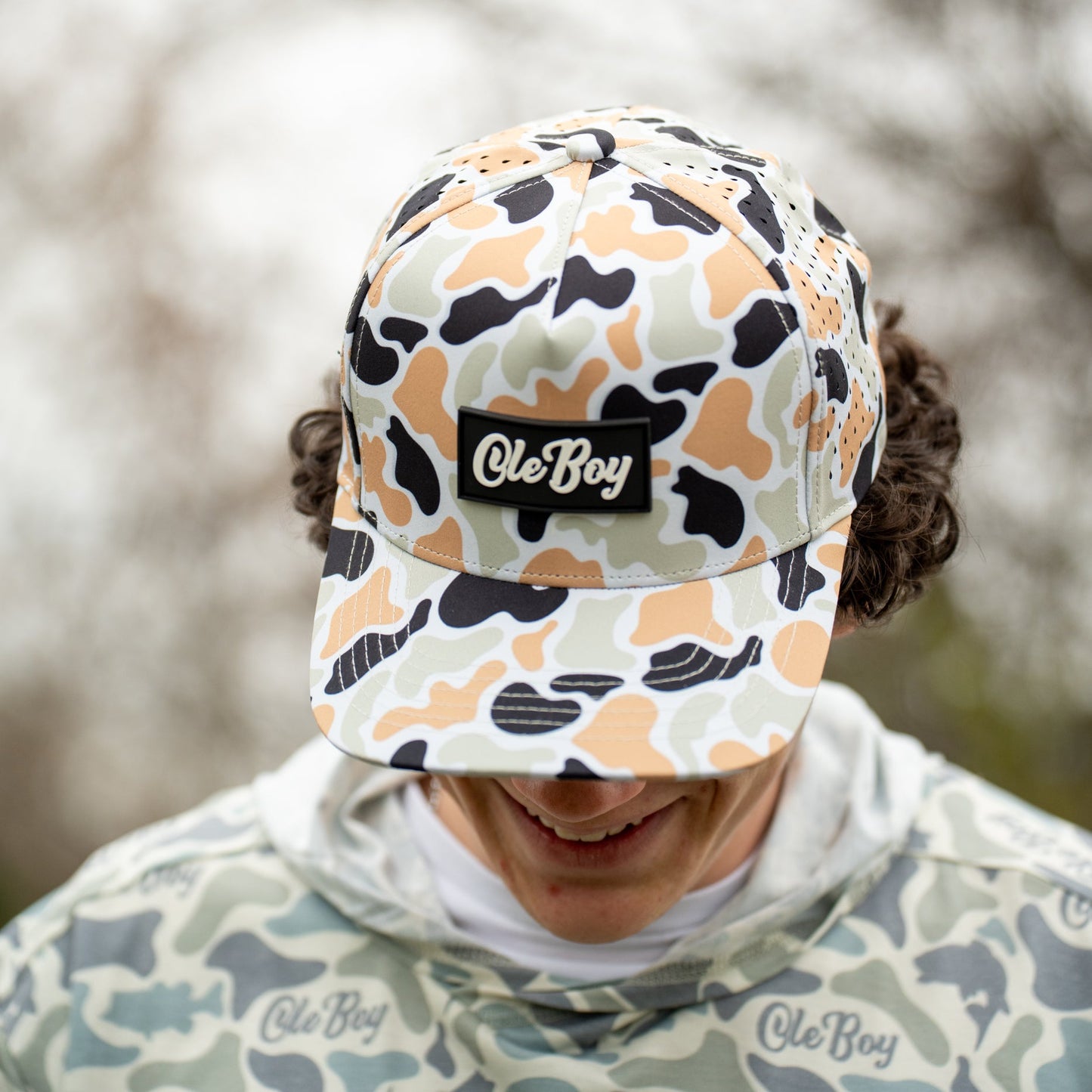 Person wearing a camouflage cap with 'Ole Boy' branding against a blurred natural background.