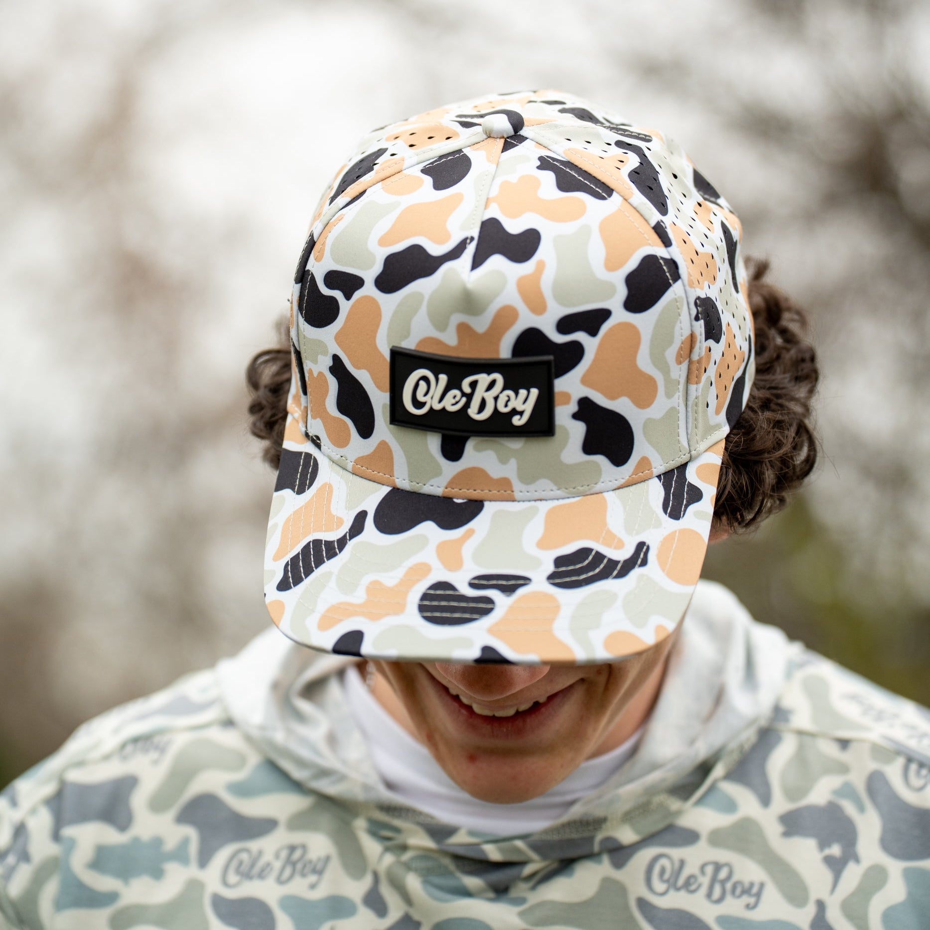 Person wearing a camouflage cap with 'Ole Boy' branding against a blurred natural background.