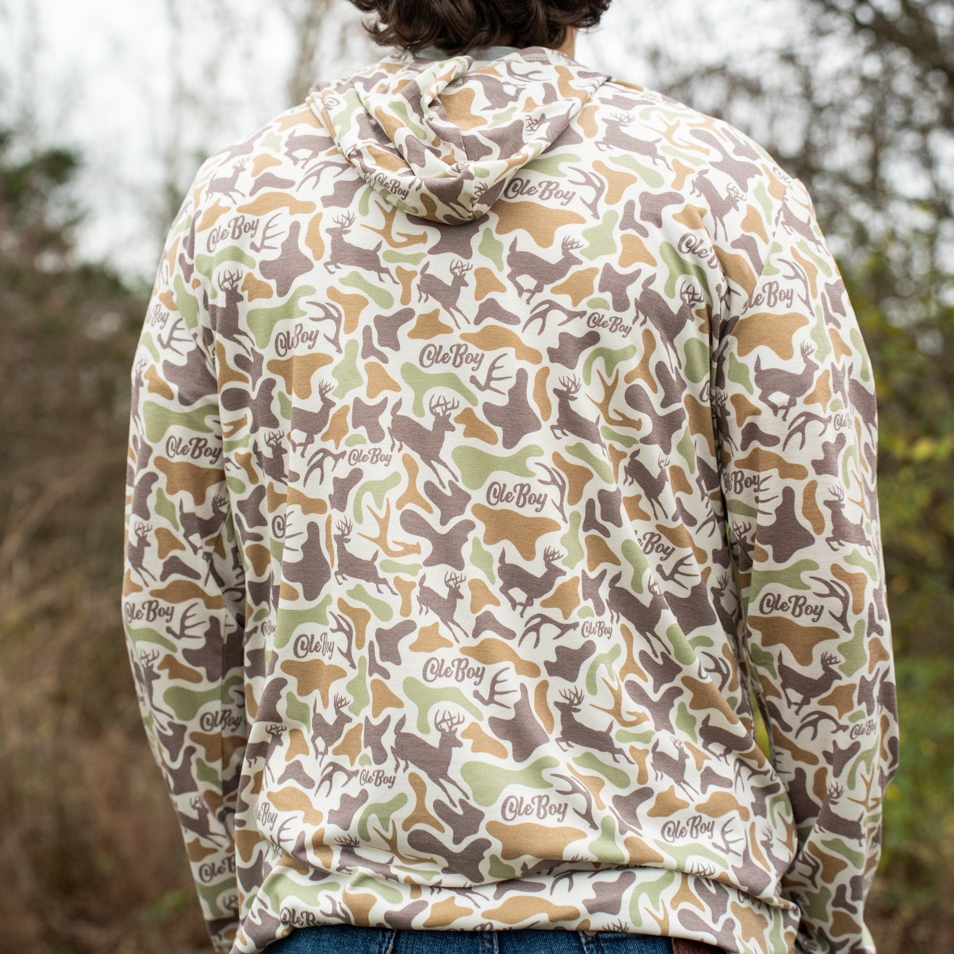 Person wearing a camouflage hoodie with a brand logo, standing in a natural setting.