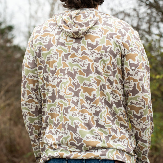 Person wearing a camouflage hoodie with a brand logo, standing in a natural setting.