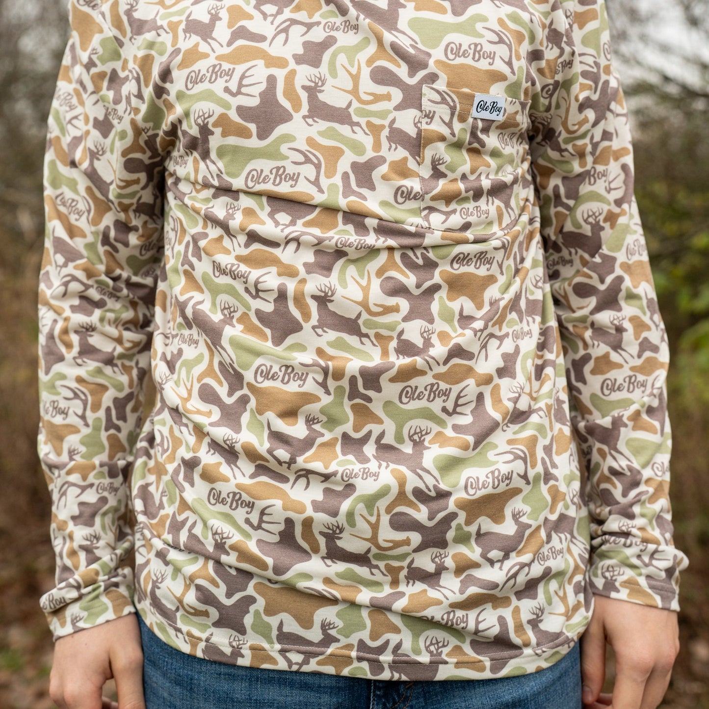 Person wearing a camouflage long-sleeve shirt with brand logos outdoors.