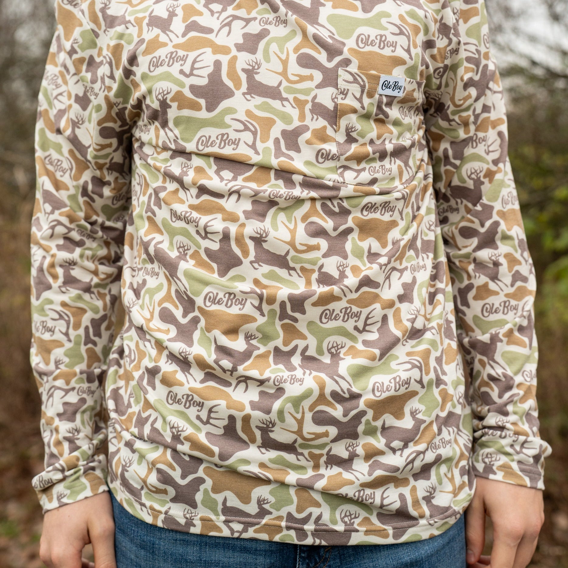 Person wearing a camouflage long-sleeve shirt with brand logos outdoors.