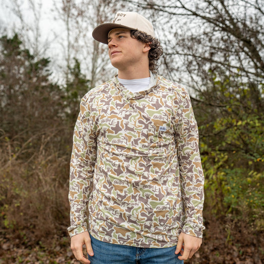 Person wearing a camouflage long-sleeve shirt and cap outdoors with trees in the background