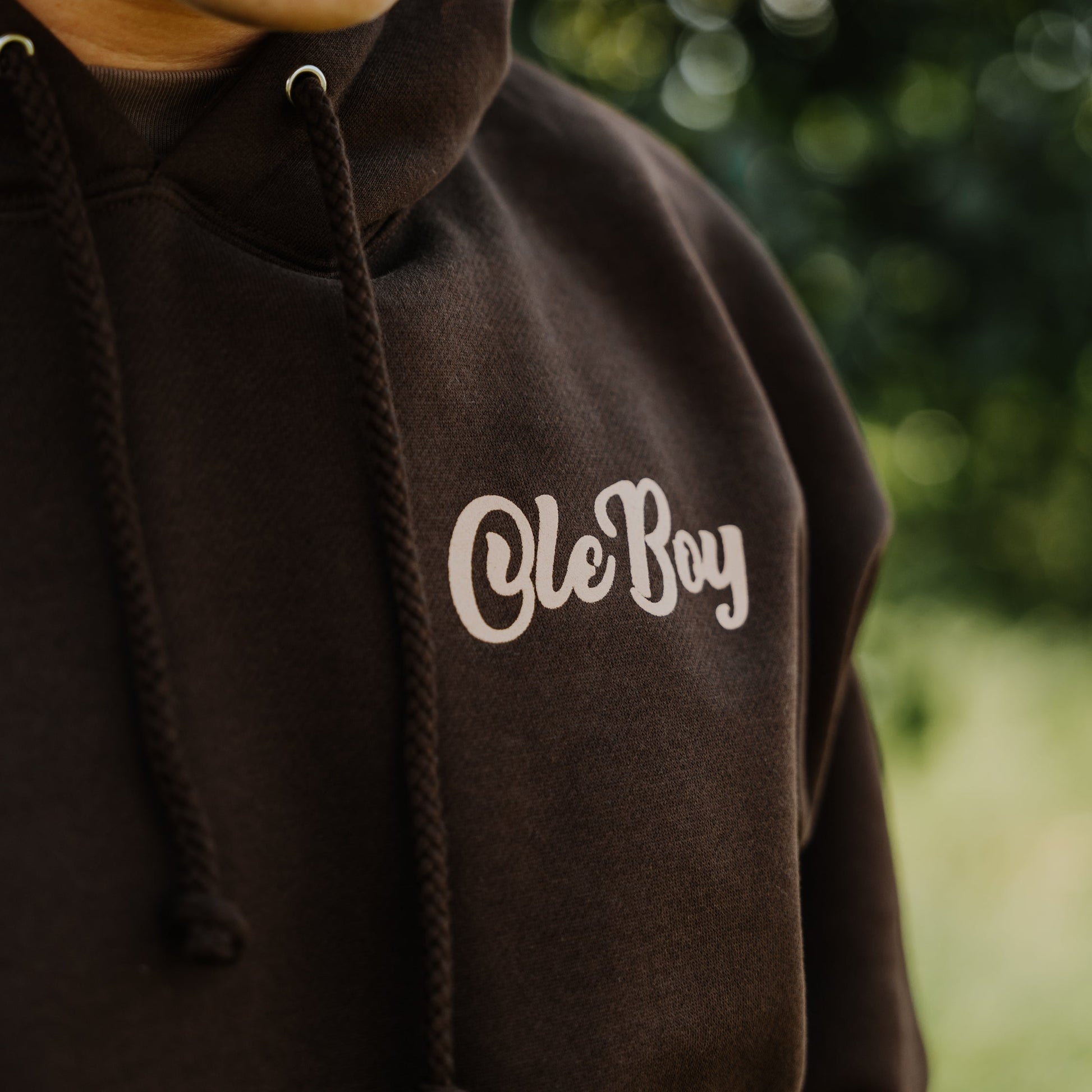 Brown hoodie with 'Ole Boy' text on a blurred green background