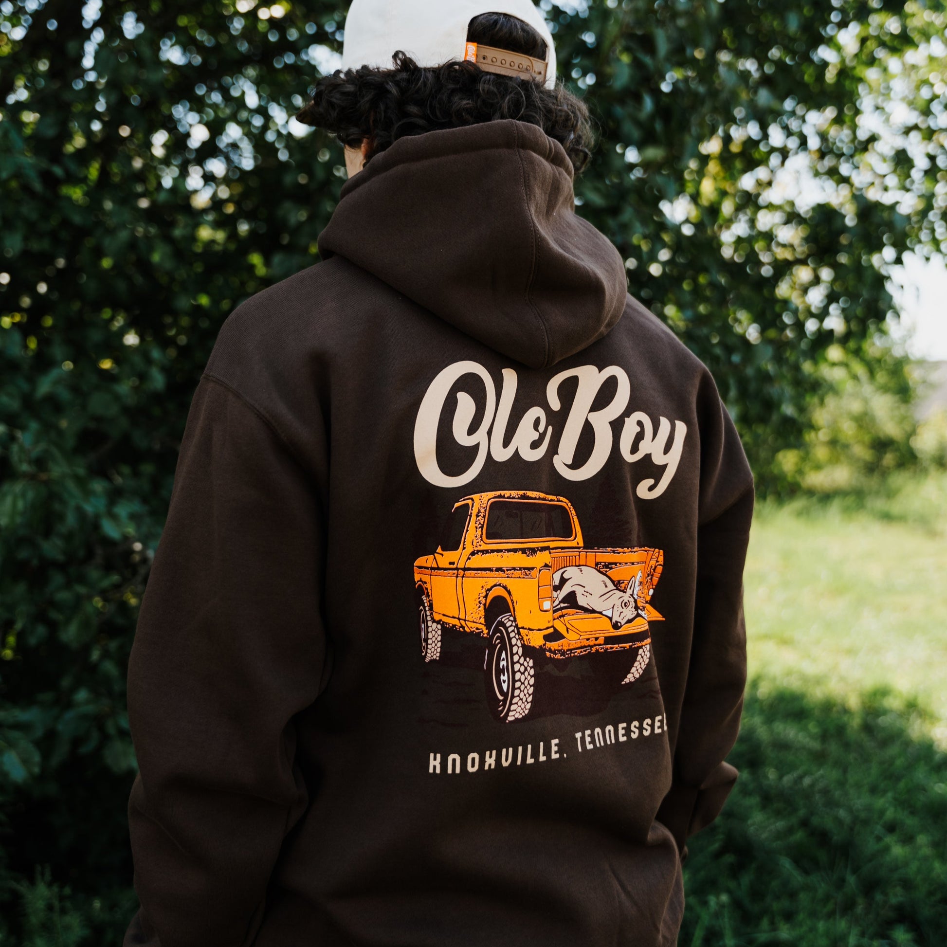 Person wearing a black hoodie with 'Ole Boy' graphic design outdoors.