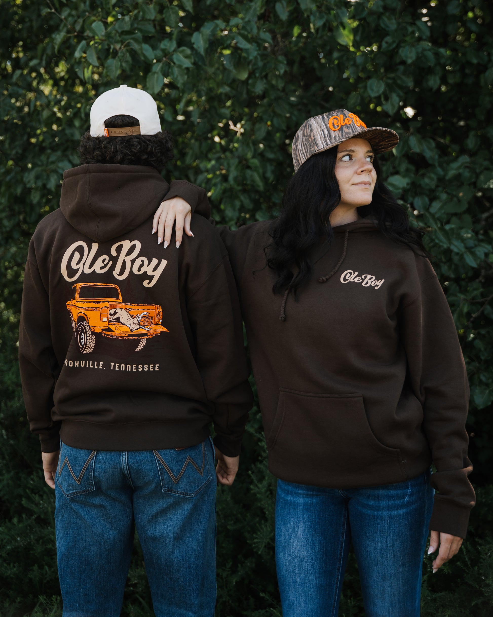 Two people wearing brown hoodies with 'Ole Boy' branding, one with a graphic of an orange truck on the back.