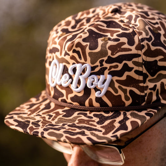 Camouflage-patterned cap with 'Ole Boy' text held by a person against a blurred natural background