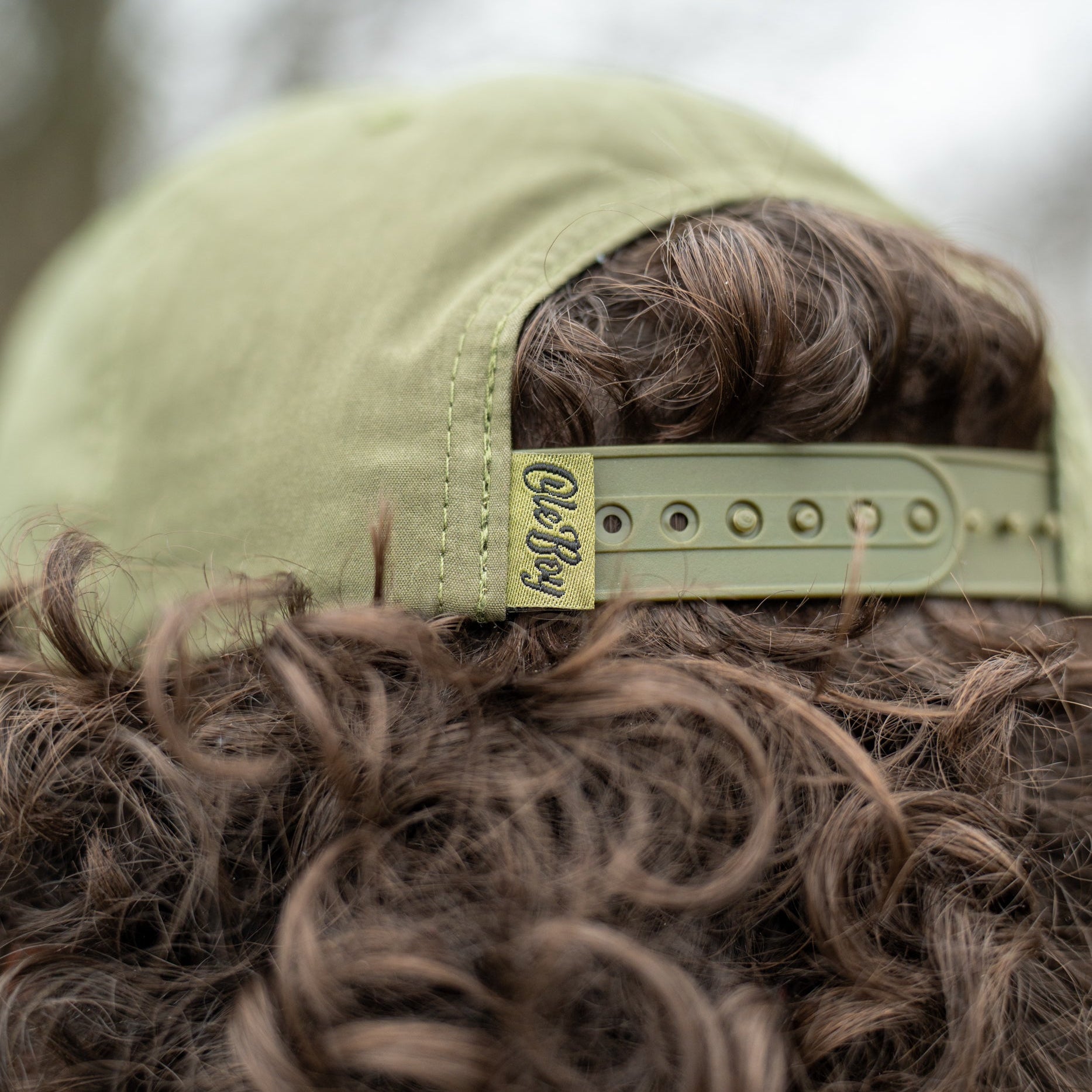 Close-up of a person wearing a green cap with a brand logo, blurred background