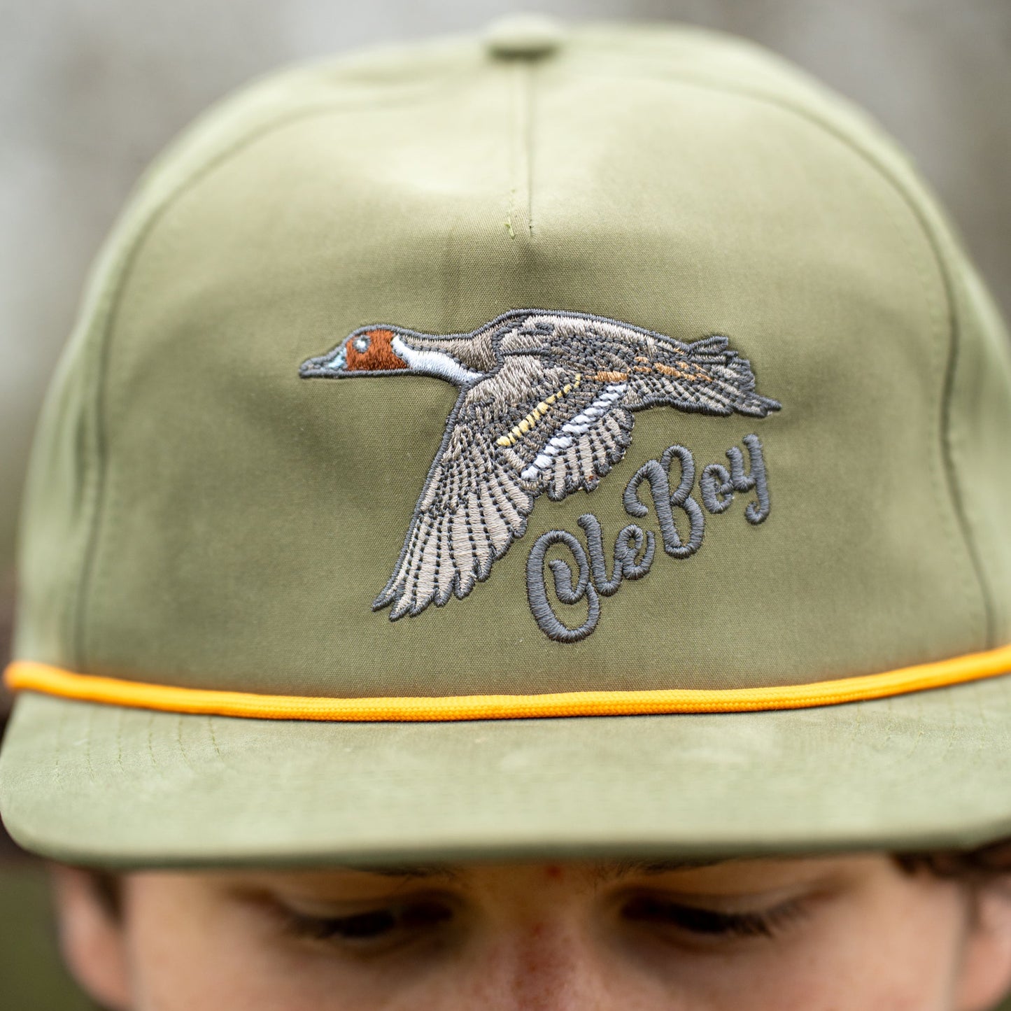 Green cap with a duck logo and 'Ole Boy' text worn by a person, blurred background