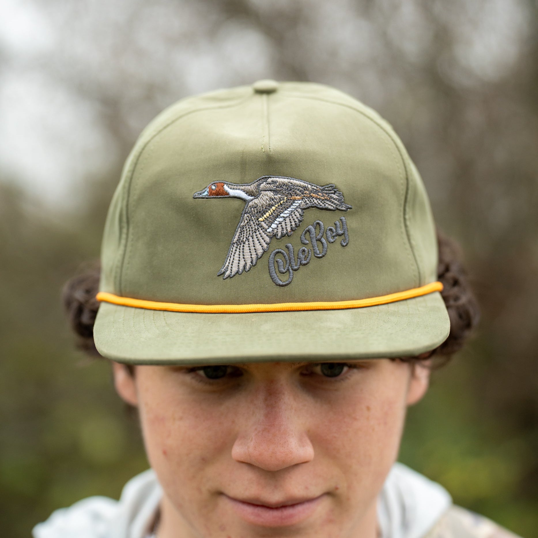 Person wearing a green cap with a logo against a blurred natural background