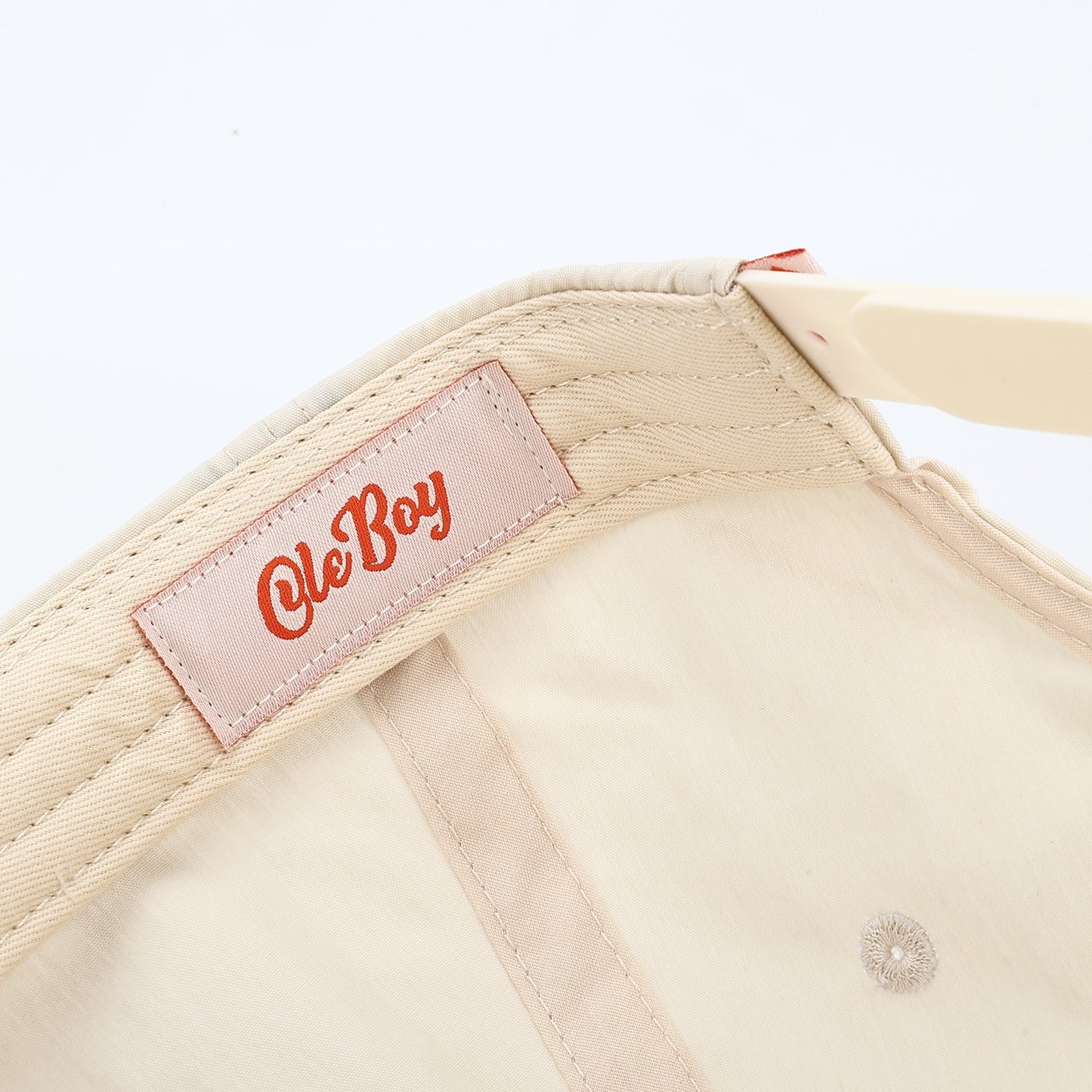 Close-up of a beige cap with a 'Ole Boy' label on a white background