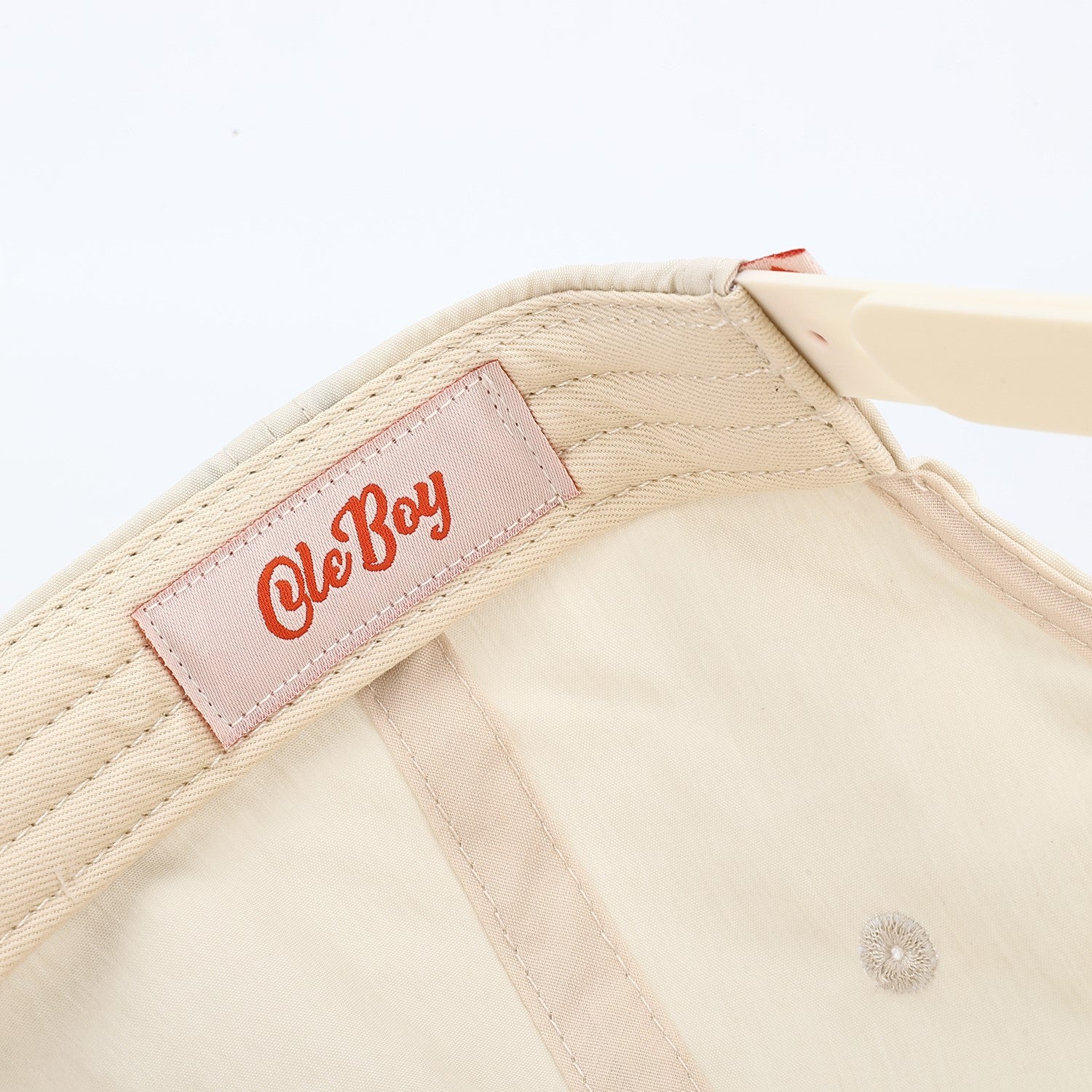 Close-up of a beige cap with a 'Ole Boy' label on a white background