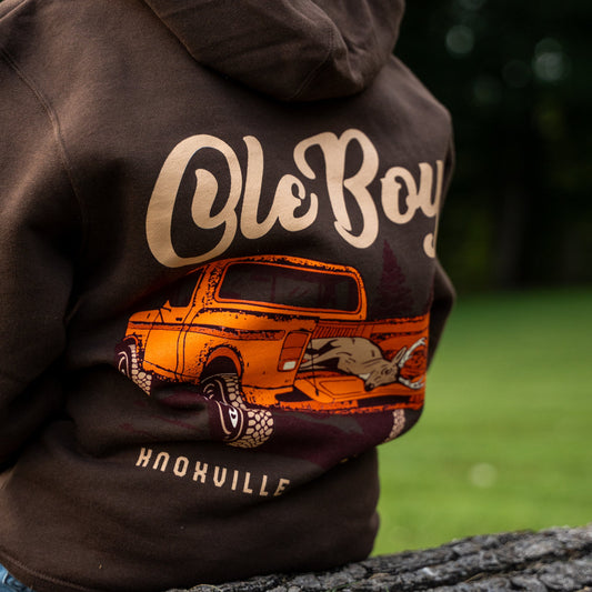 Brown hoodie with 'Ole Boy' and truck graphic on a blurred green background
