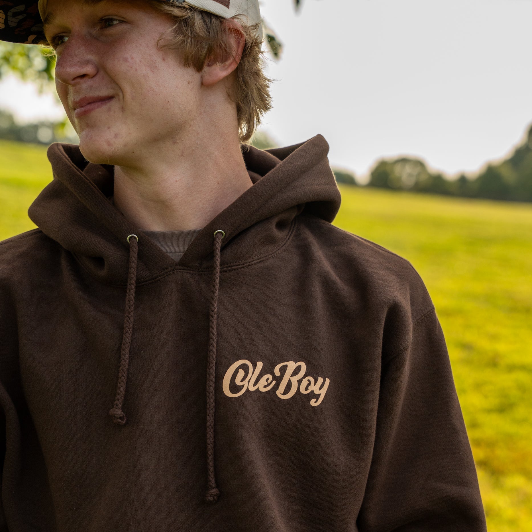 Person wearing a brown hoodie with 'Ole Boy' text in a field