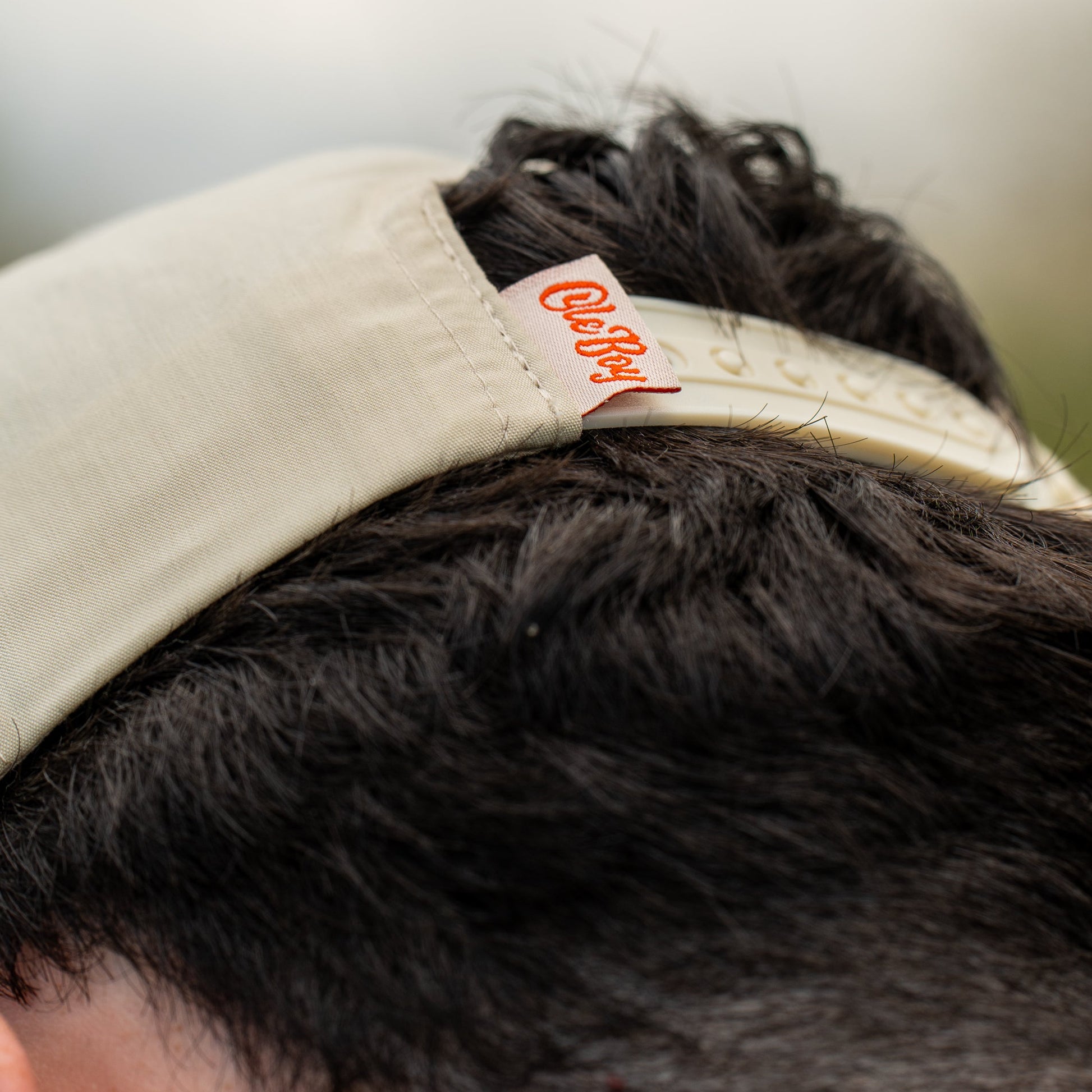 Close-up of a beige cap with an ole boy brand tag on dark hair