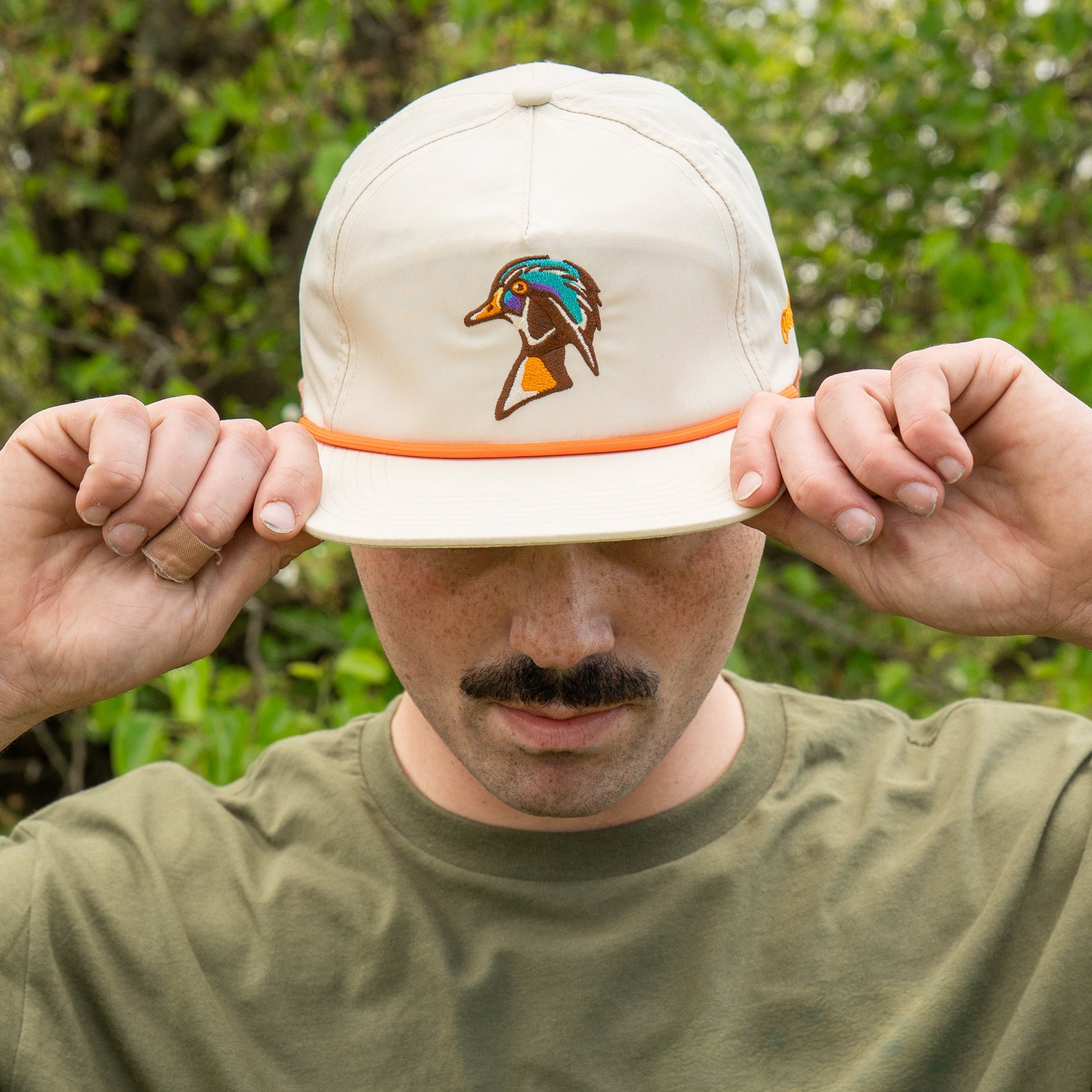 Person wearing a beige cap with a logo, adjusting it outdoors.