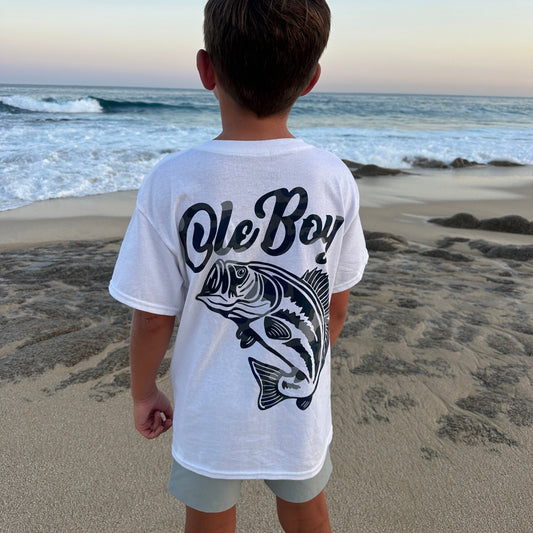 Person wearing a white t-shirt with 'Ole Boy' Bass fish design on a beach