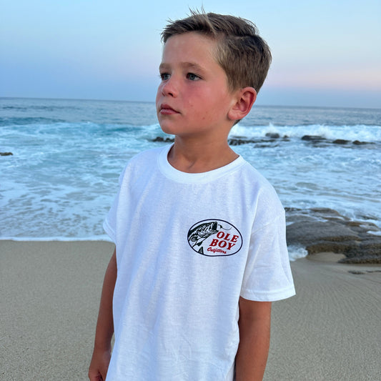 Child wearing a white t-shirt with a ole boy logo on a beach