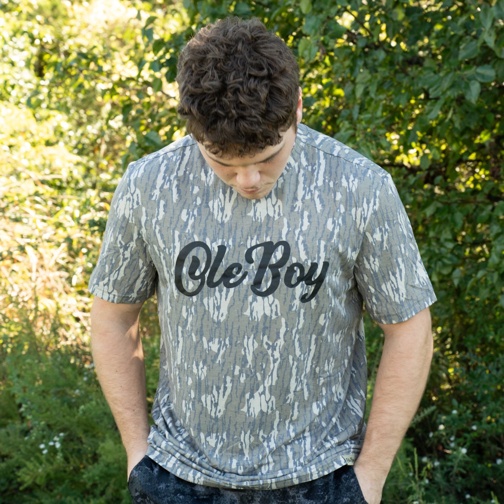Person wearing a camo 'Ole Boy' t-shirt outdoors with greenery in the background