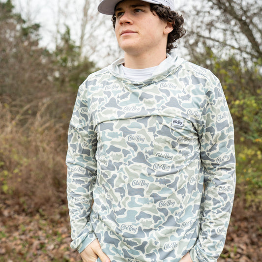 Person wearing a camouflage-patterned shirt with brand logos outdoors