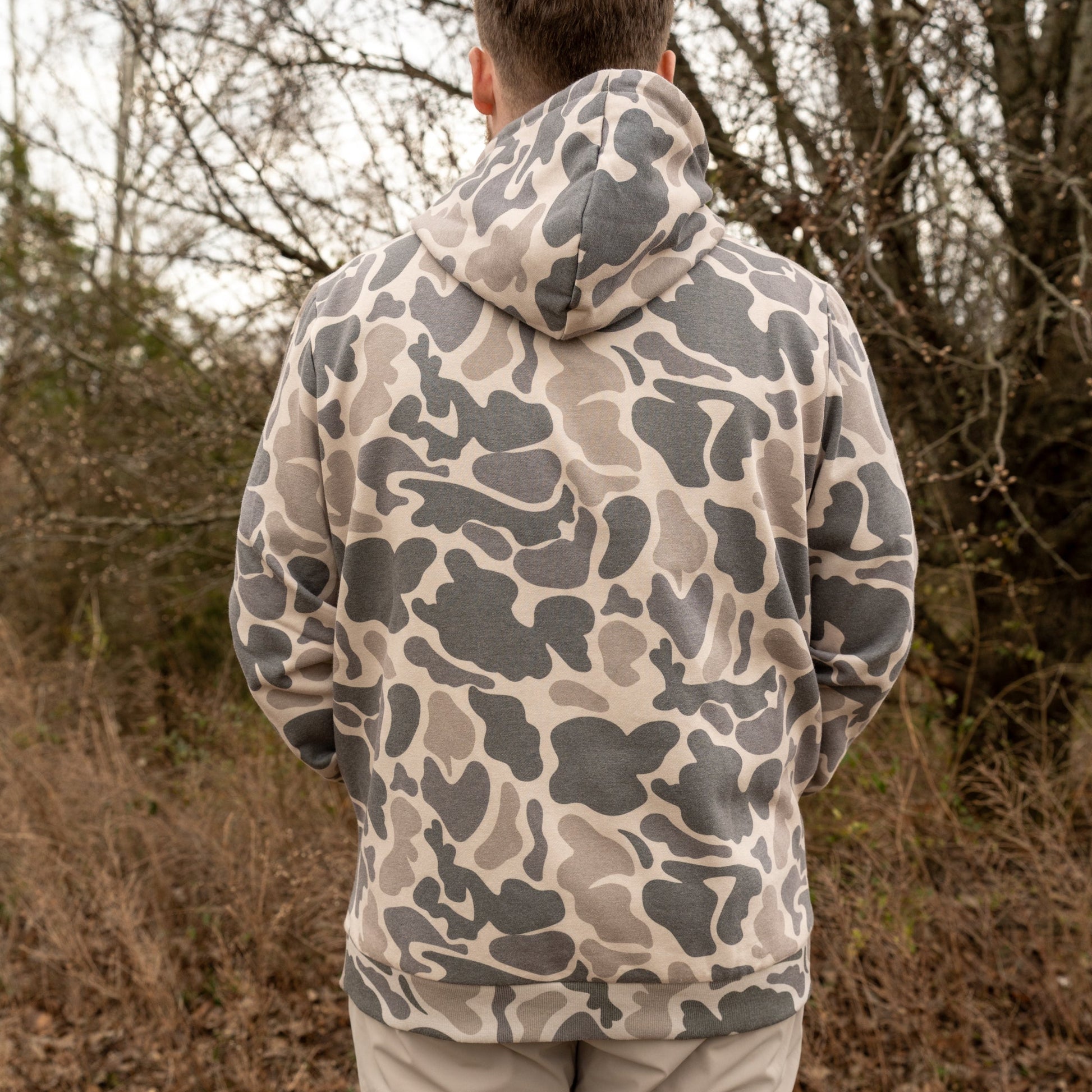 Person wearing a camouflage hoodie standing in a forested area