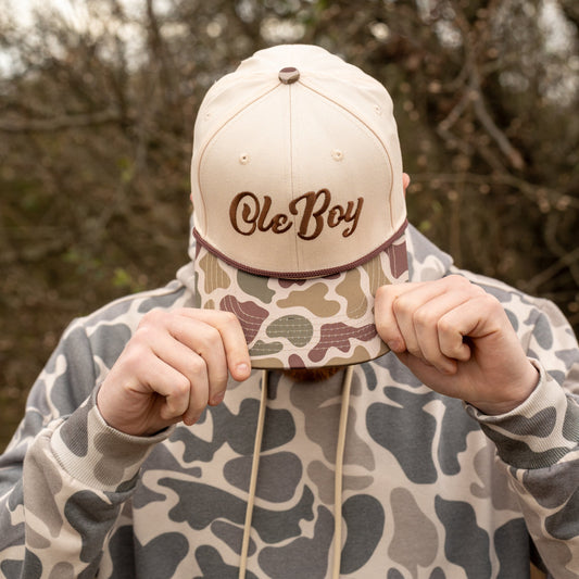 Person holding a cap with 'Ole Boy' text in a natural setting