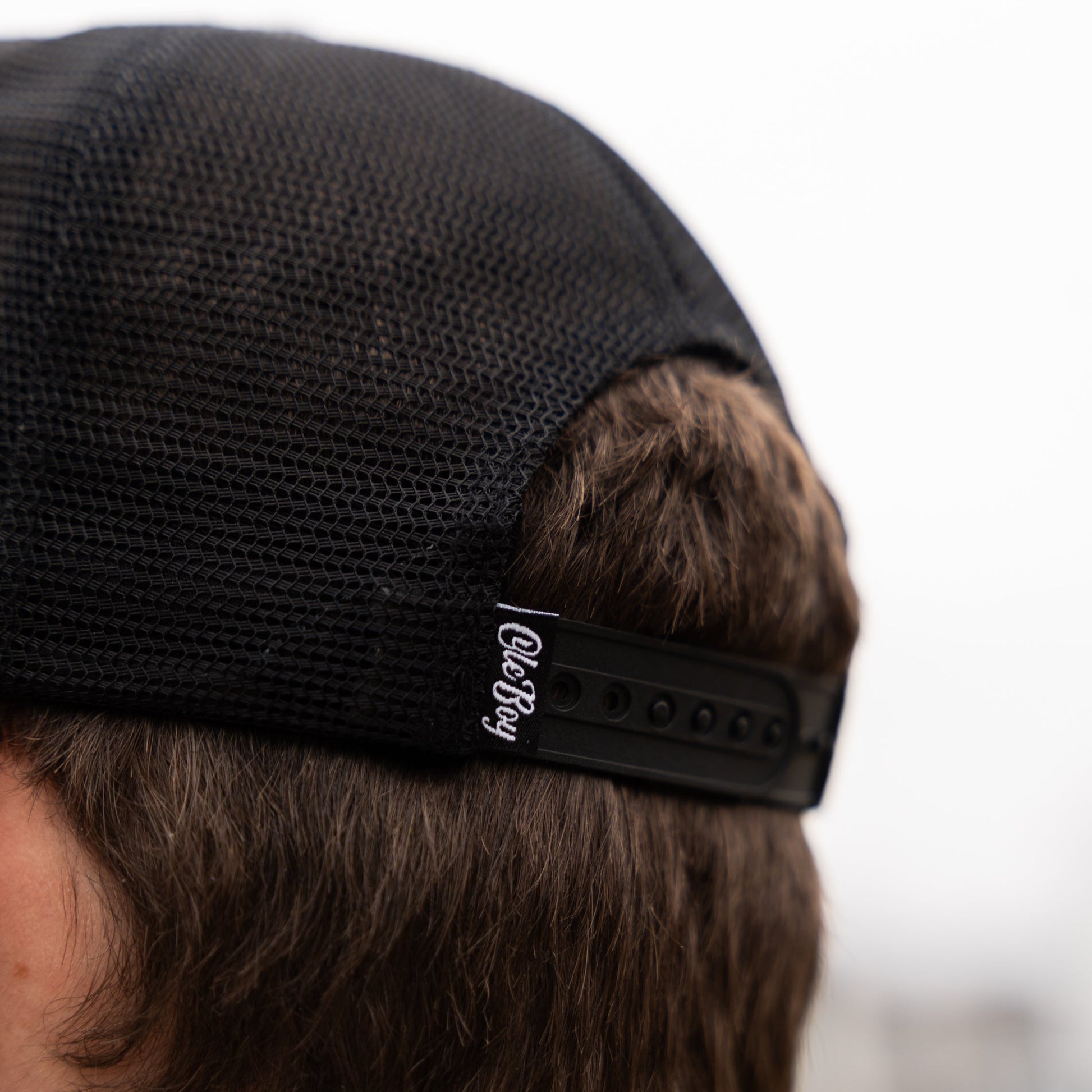 Black cap with a brand logo on the back, worn by a person with brown hair.
