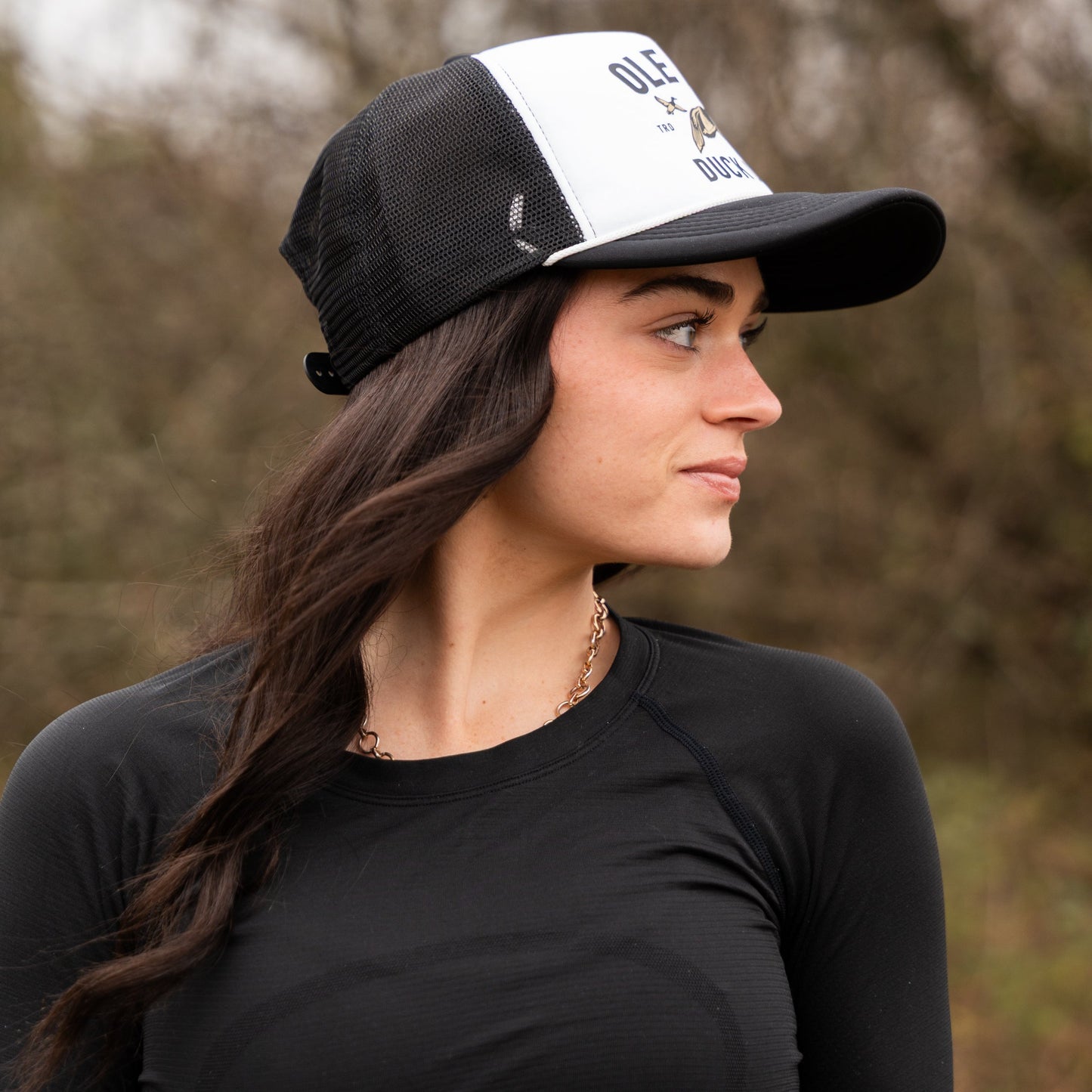 Woman wearing a black and white cap with text, standing outdoors.