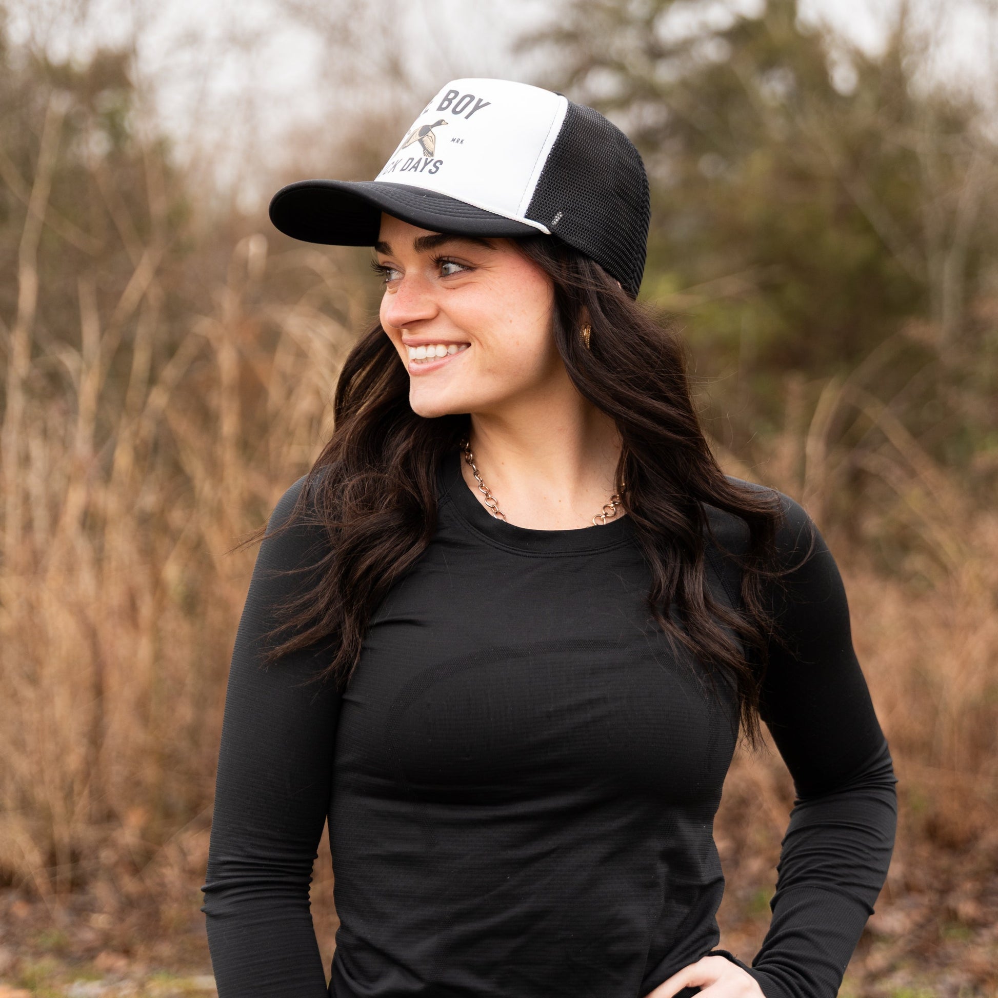 Woman wearing a black long-sleeve shirt and a black and white cap in an outdoor setting.