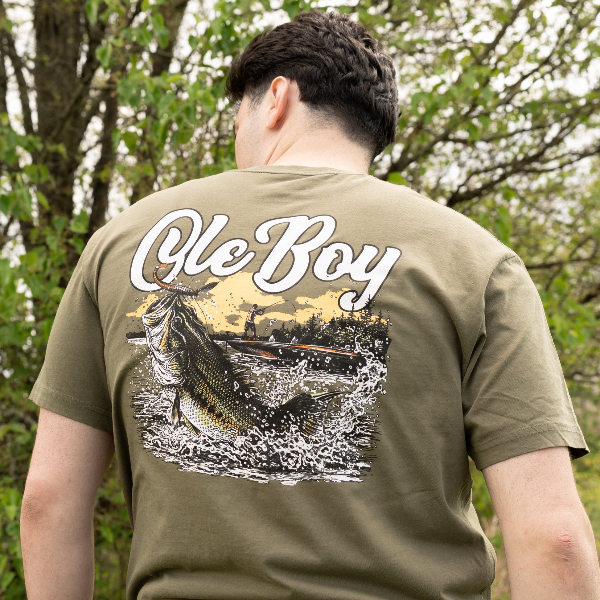 Person wearing a green t-shirt with 'Ole Boy' and a fish graphic outdoors.