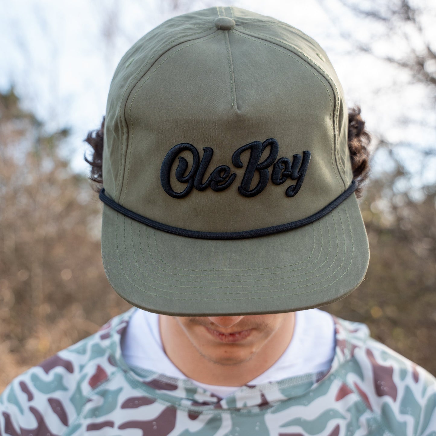 Person wearing a green cap with 'Ole Boy' text, blurred natural background