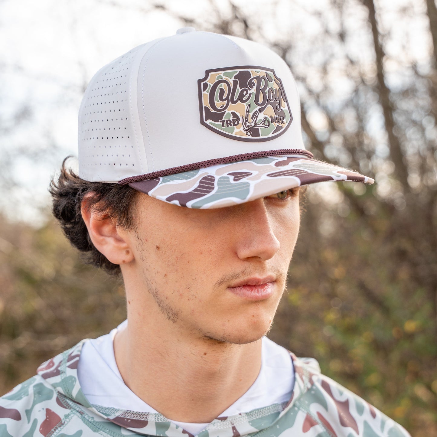 Person wearing a camouflage hoodie and a white cap with a logo outdoors