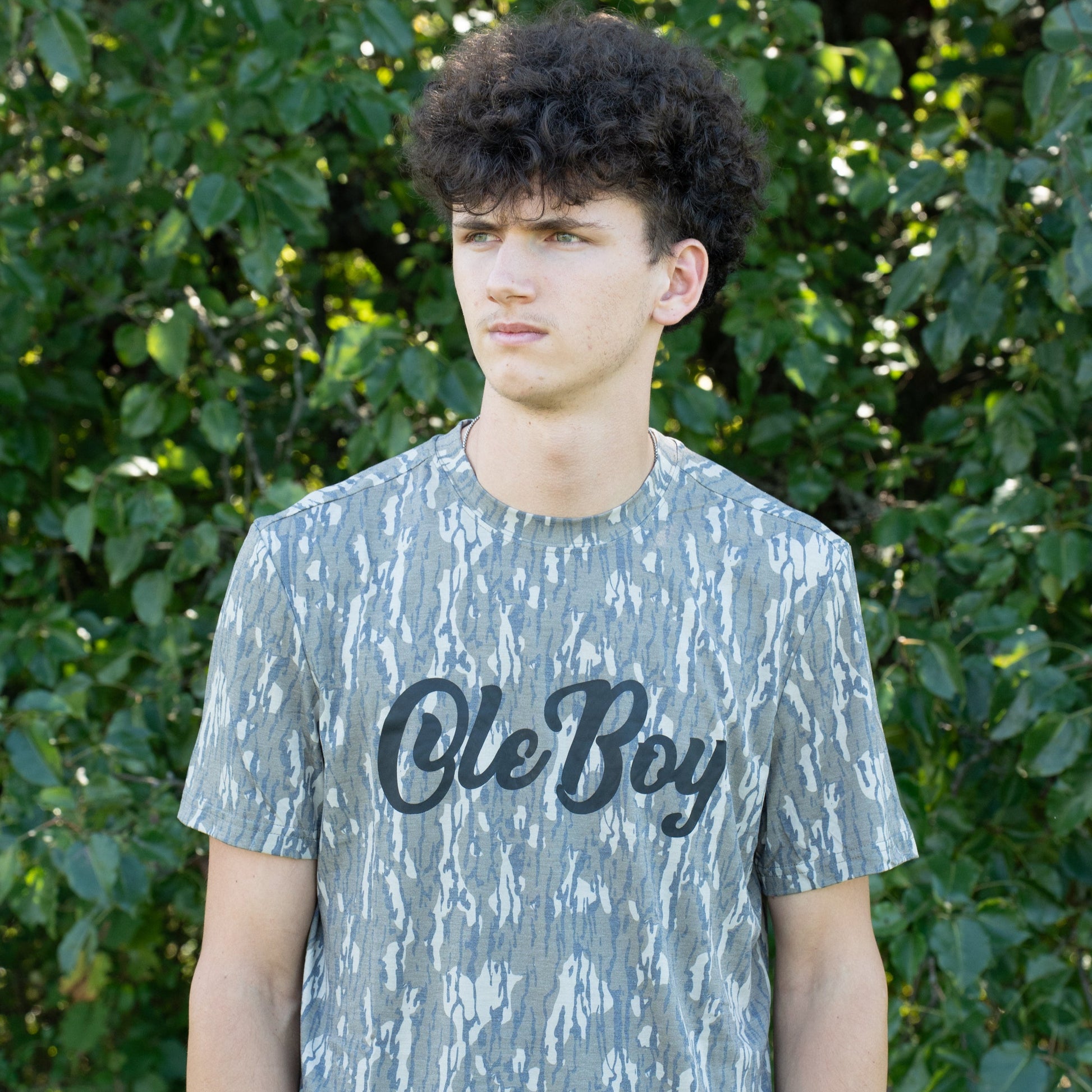 Person wearing a camouflage t-shirt with 'Ole Boy' text in front of green foliage